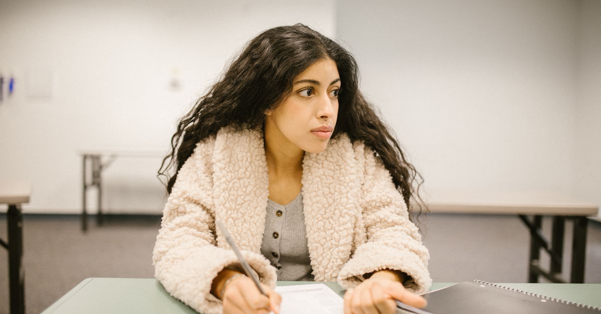 A college student writing on a test paper while looking away in a classroom setting.